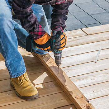 A man operates a drill while constructing a wooden deck