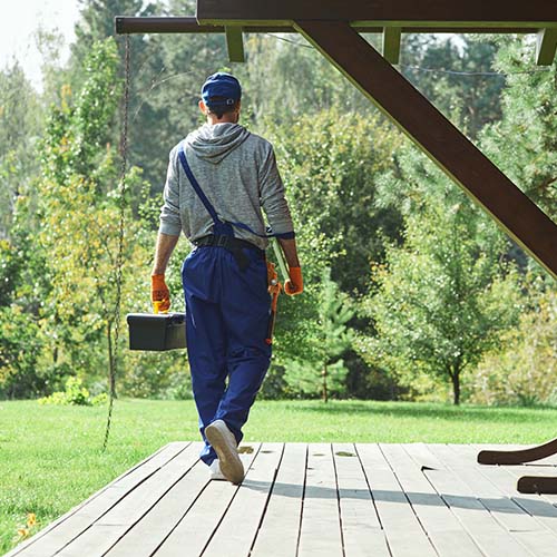 A man walks on a wooden deck, carrying various tools